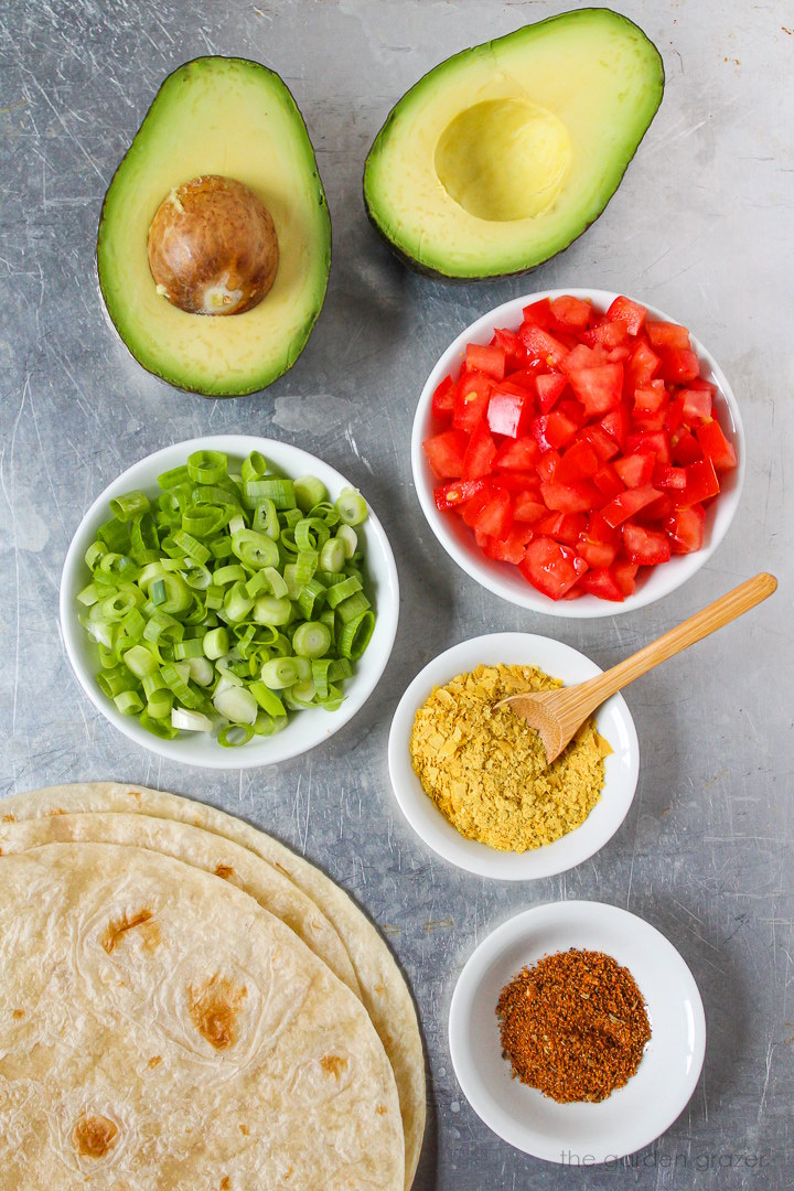 Diced tomato, green onions, tortillas, nutritional yeast, and seasoning ingredients laid out on a metal tray