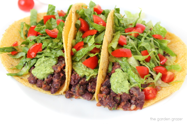 Three vegan tacos with avocado cilantro-lime sauce on a white plate