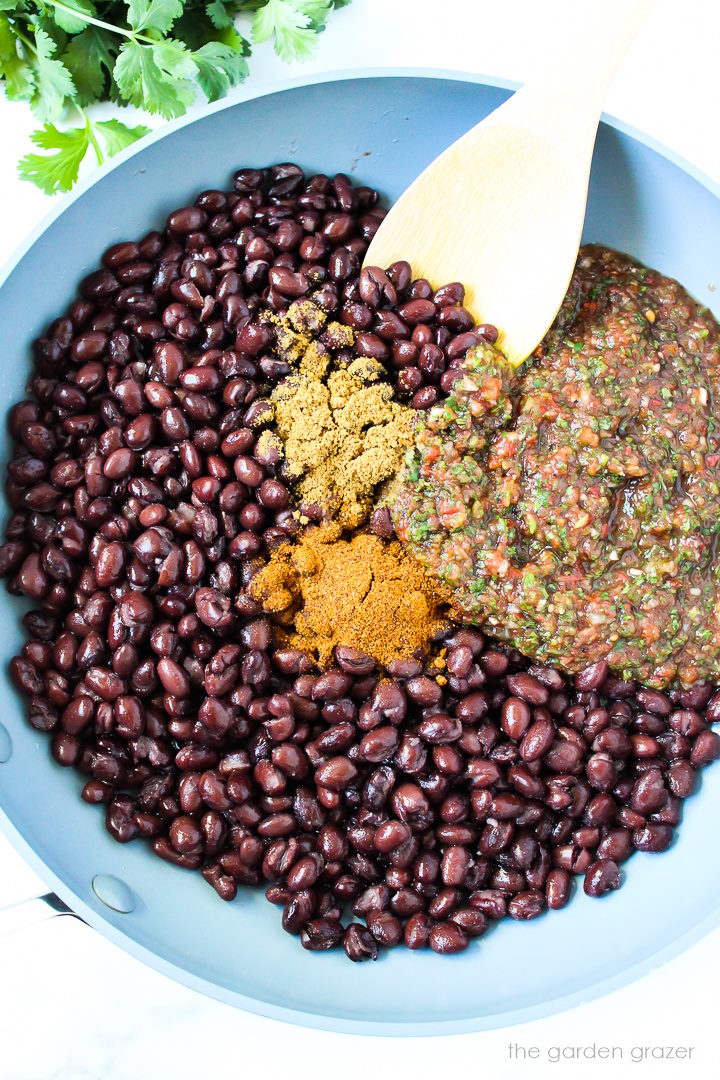 Overhead view of preparing black bean mixture in a skillet before cooking
