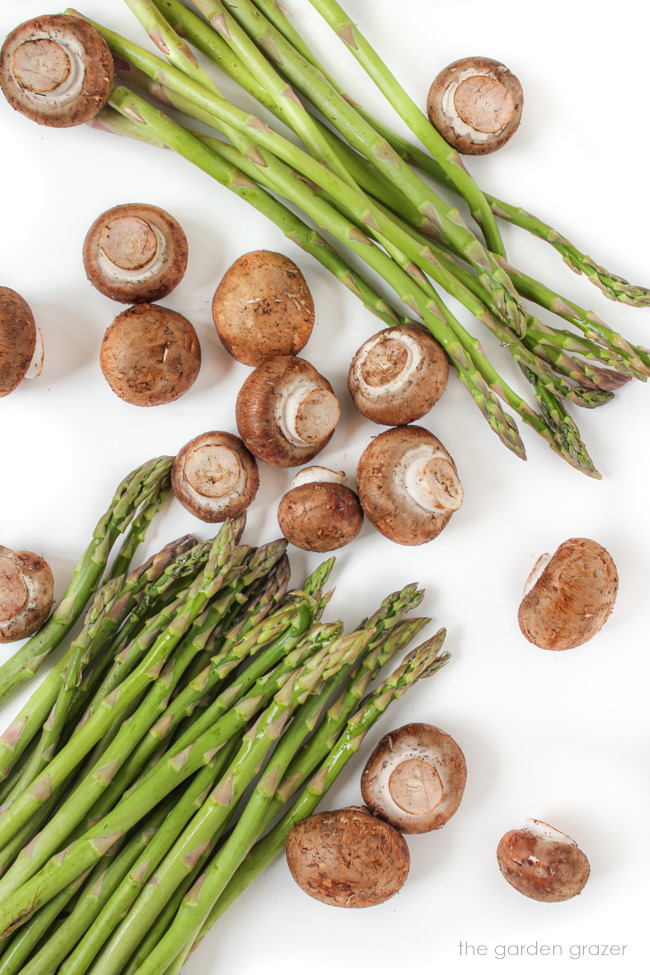 Raw fresh asparagus spears and cremini mushroom ingredients on a white table