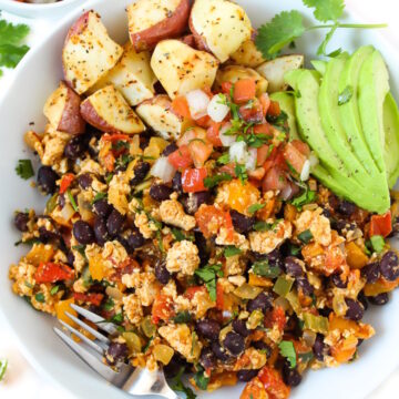 Overhead view of southwest tofu scramble in a white bowl with roasted potatoes, salsa, and avocado slices