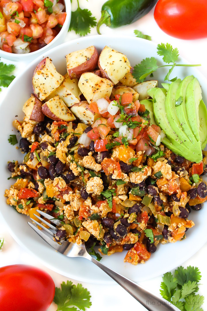 Overhead view of southwest tofu scramble in a white bowl with roasted potatoes, salsa, and avocado slices