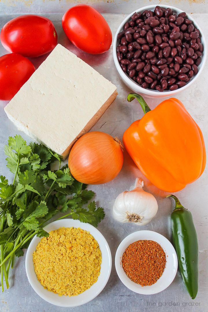 Black beans, bell pepper, onion, garlic, tomato, and spice ingredients laid out on a metal tray