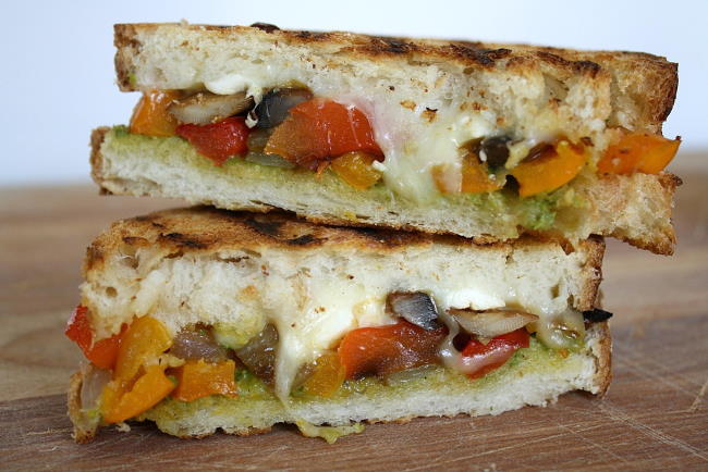 Roasted Vegetable Panini with pesto cut in half on a cutting board