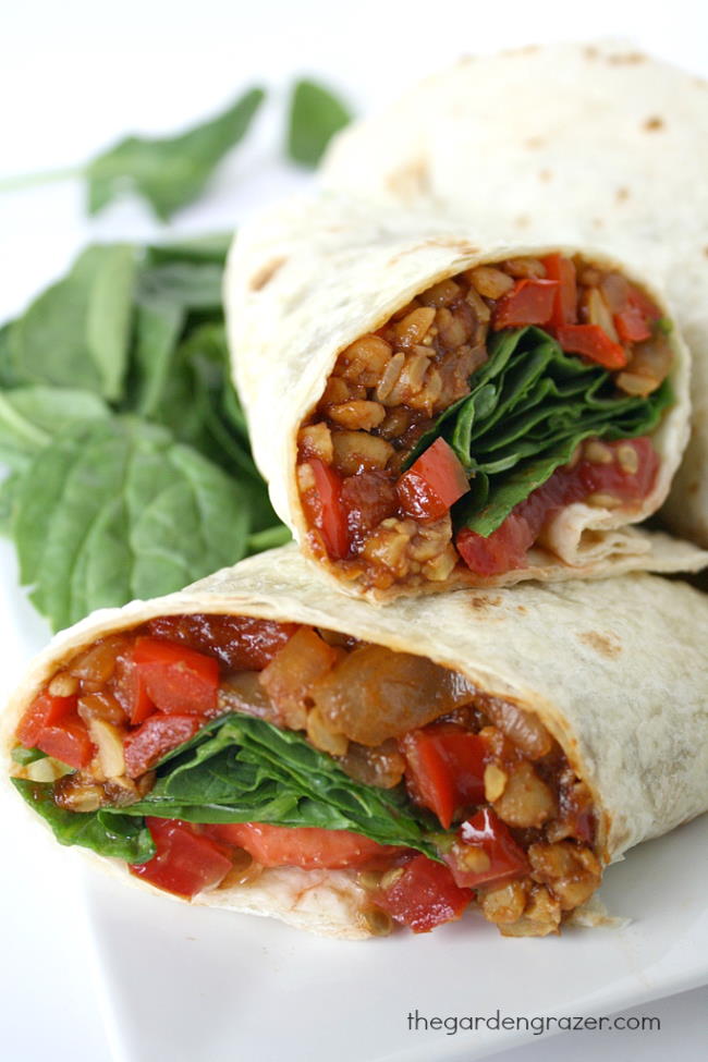 Vegan BBQ tempeh wrap halves on a plate with spinach