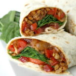 Vegan tempeh wraps with spinach and tomato cut in half on a plate