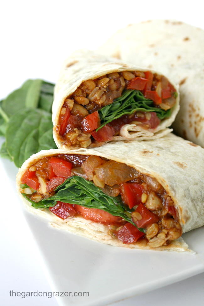 Vegan tempeh wraps with spinach and tomato cut in half on a plate