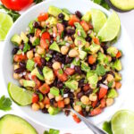 Overhead view of vegan fiesta bean salad with cumin-lime dressing in a white bowl with lime slices