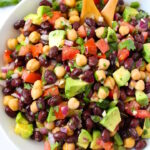 Fiesta bean salad with cumin lime dressing in a white serving bowl with wooden spoons