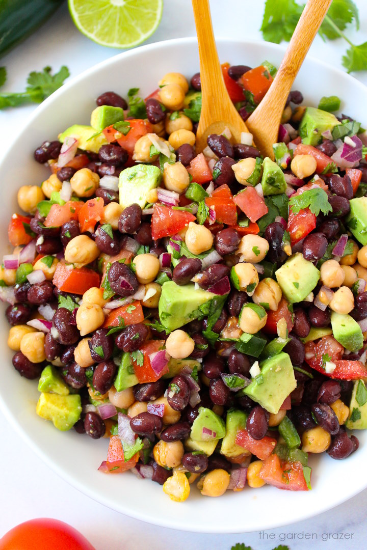Fiesta bean salad with cumin lime dressing in a white serving bowl with wooden spoons