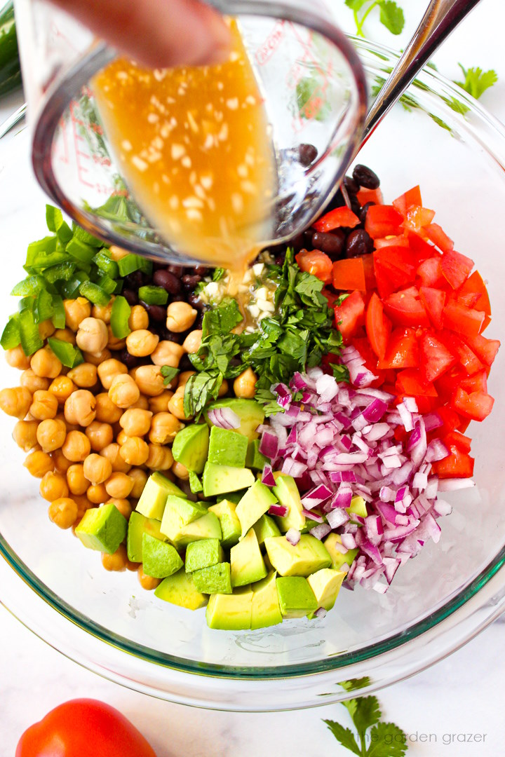 Cumin lime dressing being poured over salad ingredients in a large glass mixing bowl