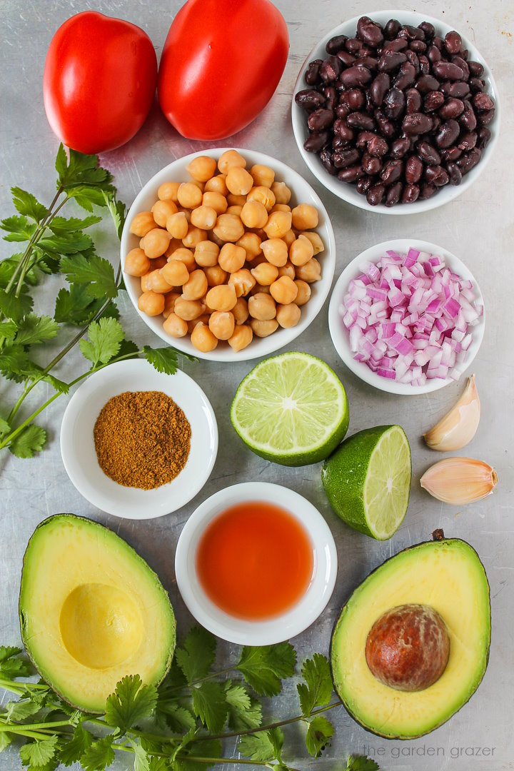 Chickpeas, black beans, onion, tomato, lime, avocado, and spice ingredients laid out on a metal tray