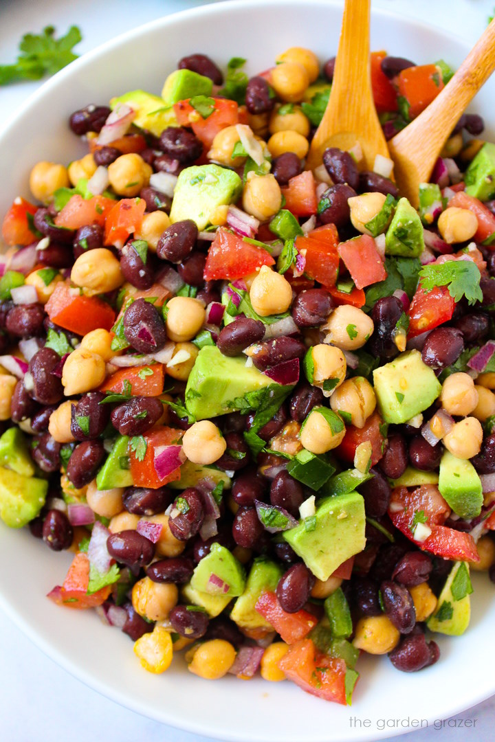 Close up view of fiesta bean salad with avocado and cilantro in a white serving bowl
