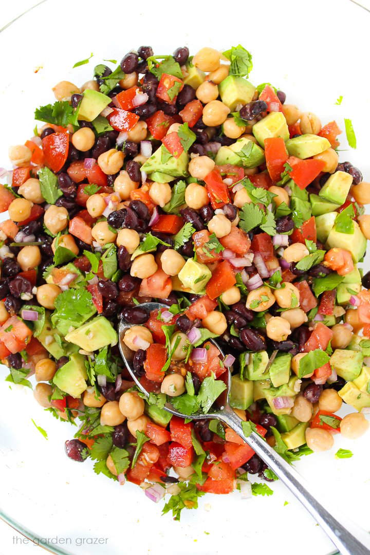 Mixing together fiesta bean salad in a large glass bowl with metal spoon