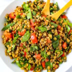 Lentil caper salad with spinach and balsamic dressing served in a white bowl with wooden spoons