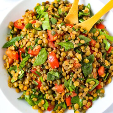 Lentil caper salad with spinach and balsamic dressing served in a white bowl with wooden spoons