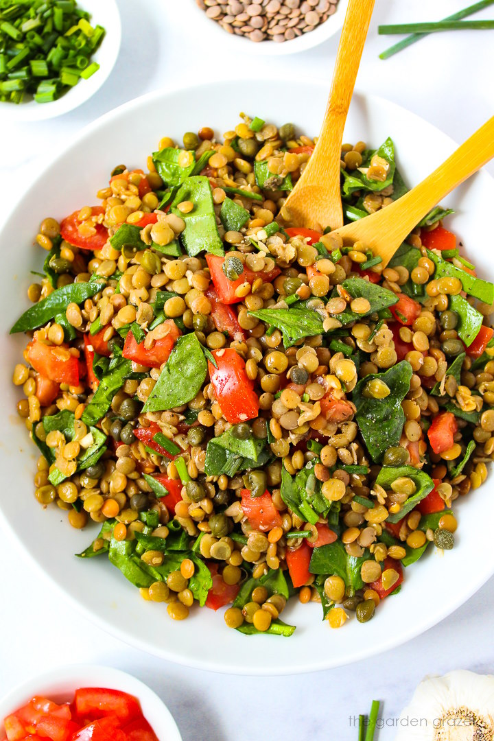 Lentil caper salad with spinach and balsamic dressing served in a white bowl with wooden spoons