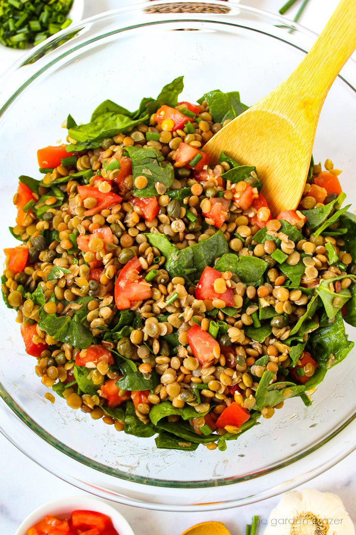 Lentil caper salad with spinach and tomatoes tossed together in a glass mixing bowl