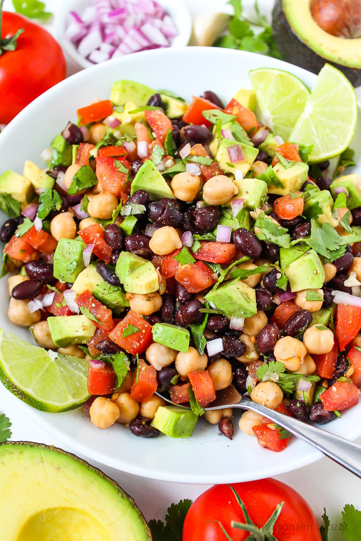 Close-up view of fiesta bean salad in a white bowl with serving spoon