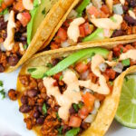 Close up view of vegan black bean tempeh tacos topped with salsa, avocado, and chipotle crema