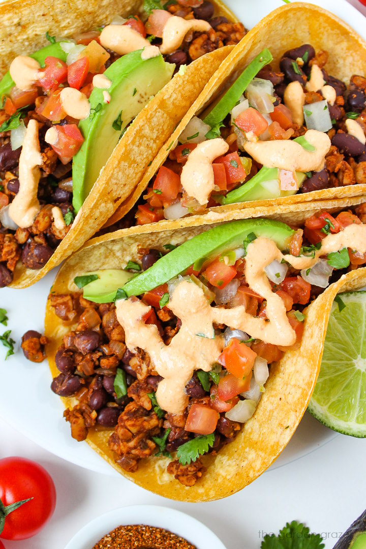 Close up view of vegan black bean tempeh tacos topped with salsa, avocado, and chipotle crema