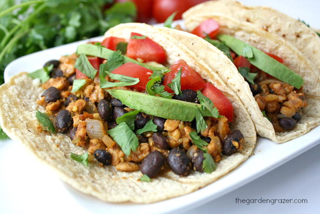 Black bean tacos with tempeh on a plate topped with avocado and tomato