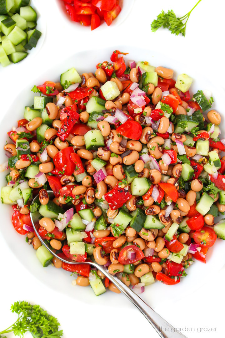 Black eyed pea salad in a white bowl with serving spoon