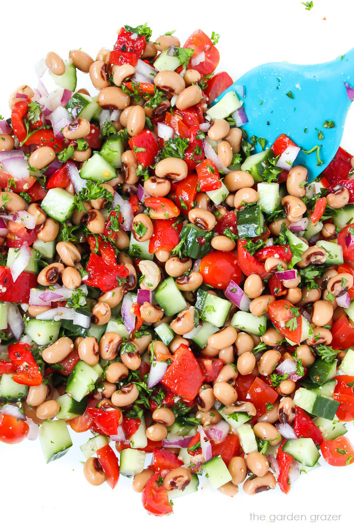 Preparing black eyed pea salad in a large glass bowl with mixing spatula