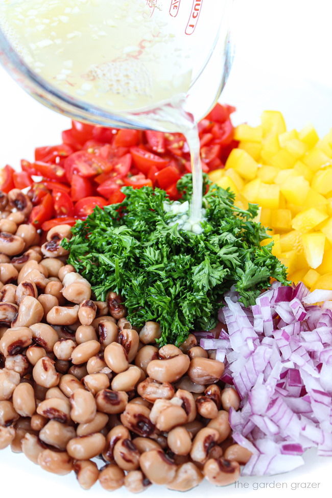 Dressing being poured over bean and veggie ingredients in a glass bowl