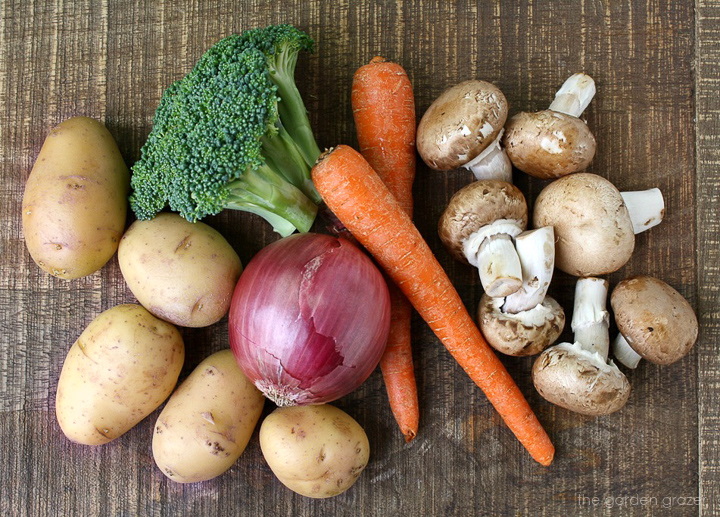 Raw potato, onion, broccoli, carrot, and mushroom ingredients in a wooden table