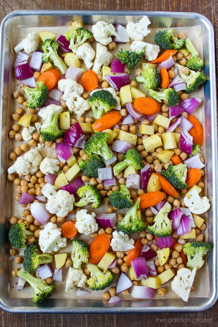Overhead view of chickpeas and vegetables tossed together on a sheet pan before roasting