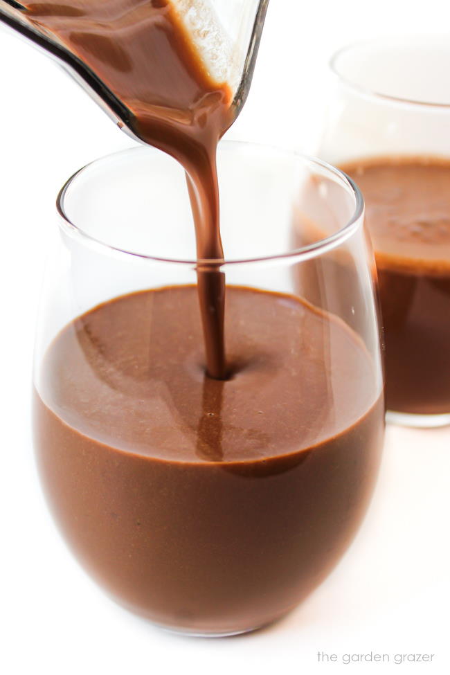 Healthy vegan chocolate milkshake being poured into glasses