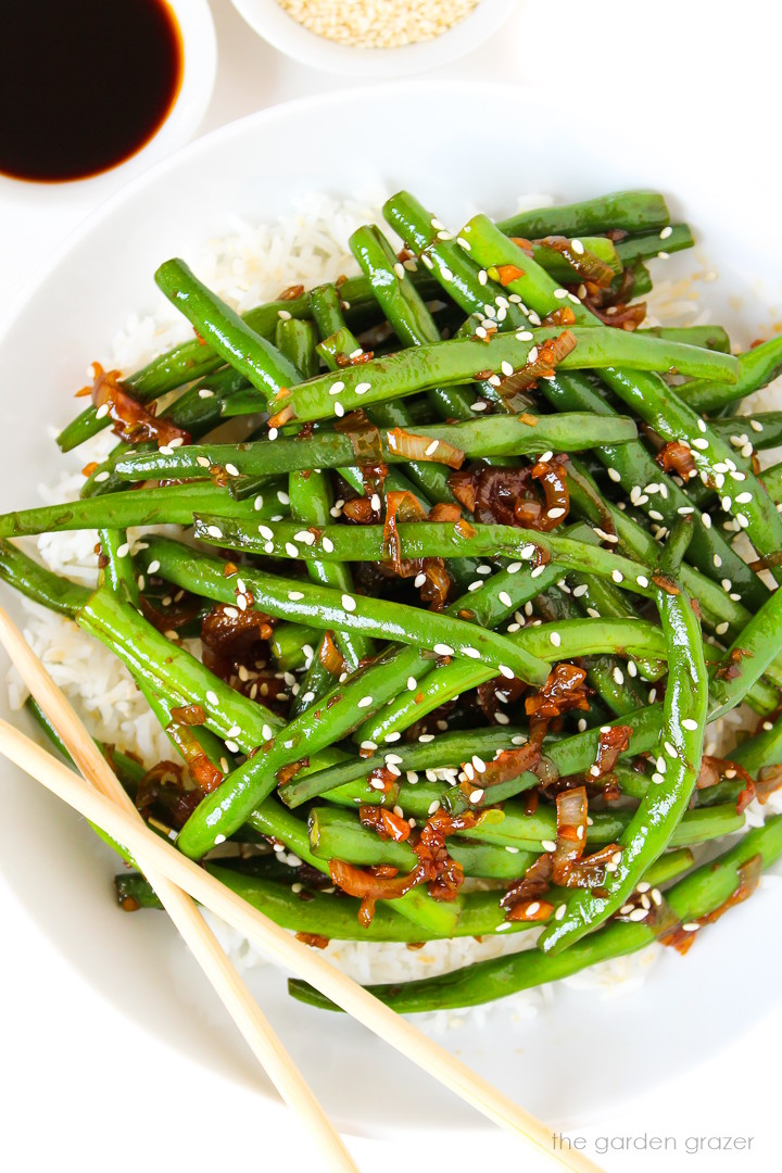 Asian-style green beans on a white plate with chopsticks and topped with sesame seeds