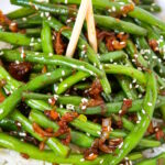 Close-up view of Asian-style garlic green beans with shallot on a white plate with chopsticks