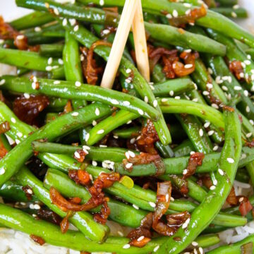 Close-up view of Asian-style garlic green beans with shallot on a white plate with chopsticks
