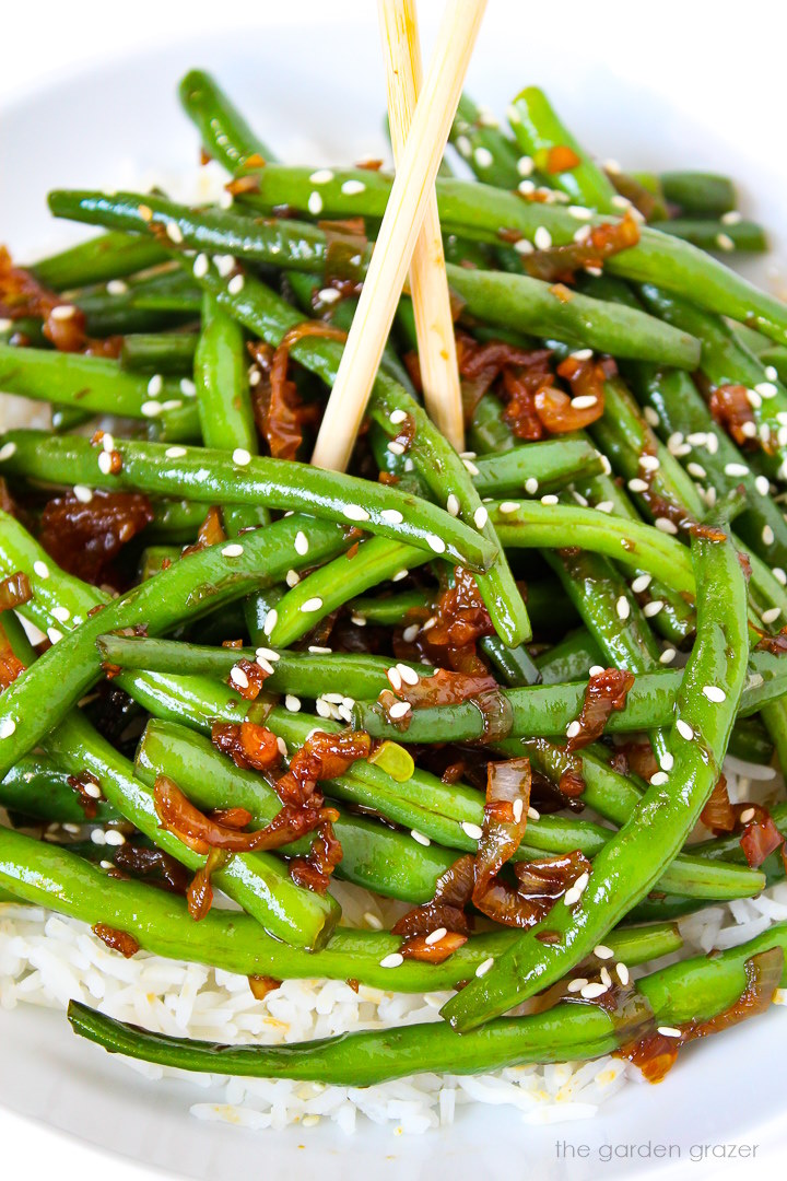 Close-up view of Asian-style garlic green beans with shallot on a white plate with chopsticks