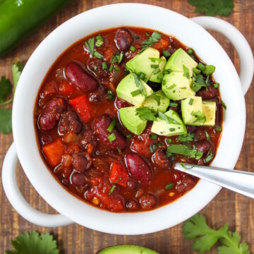 Hearty vegan chili in a white bowl topped with diced avocado, chives, and fresh cilantro
