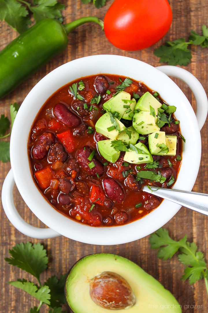 Hearty vegan chili in a white bowl topped with diced avocado, chives, and fresh cilantro