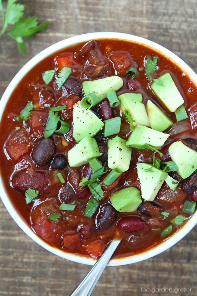 Vegan bean chili in a small white bowl topped with avocado and cilantro