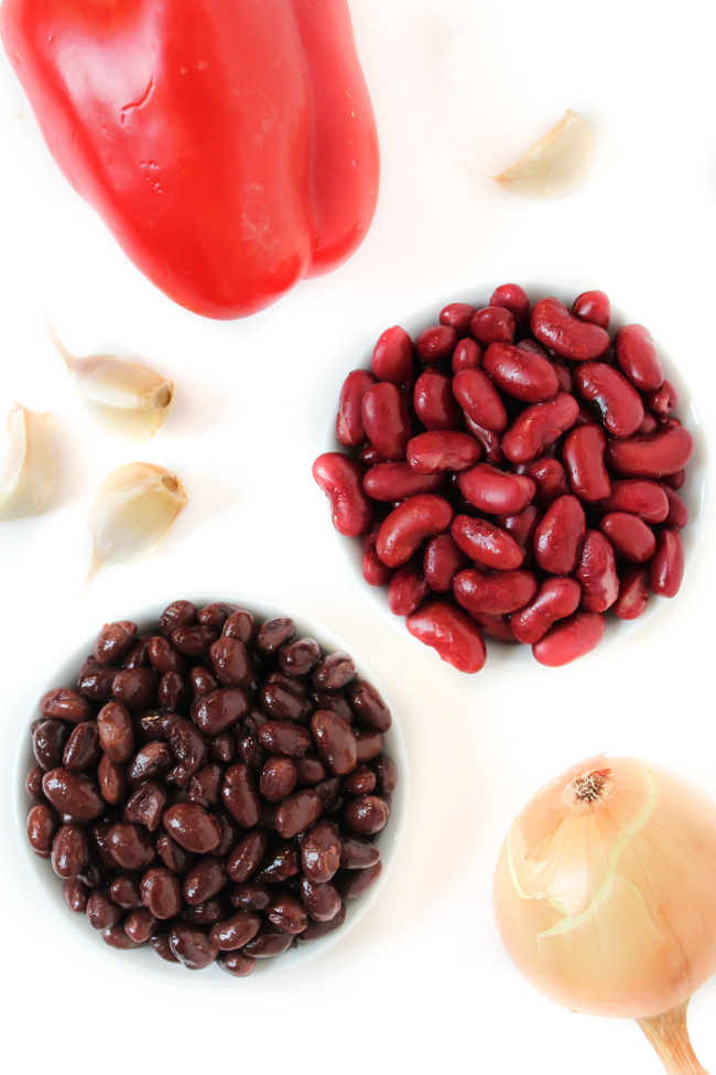 Kidney beans, black beans, red bell pepper, onion, and garlic ingredients on a white table