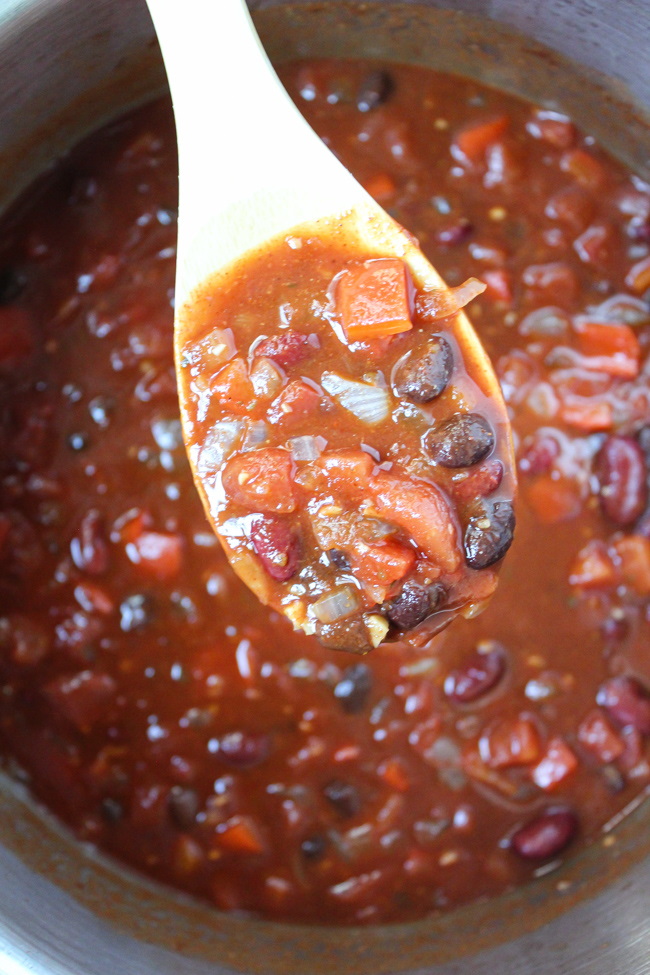 Vegan bean chili cooking in a large pot with wooden spoon