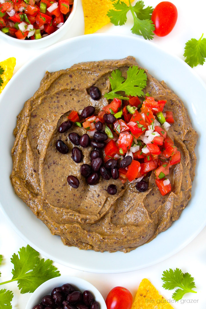 Creamy black bean avocado dip in a white serving bowl topped with beans and salsa