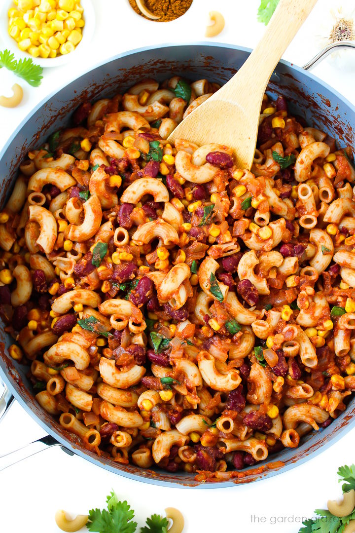Vegan chili mac cooking in a large skillet with wooden stirring spoon