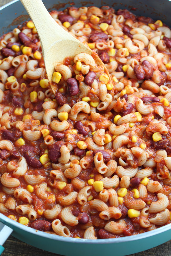 Pasta, kidney beans, and corn cooking in a pan of tomato sauce with wooden spoon