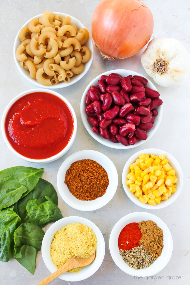 Kidney beans, elbow pasta, onion, garlic, tomato sauce, corn, spinach, and spice ingredients laid out on a metal tray