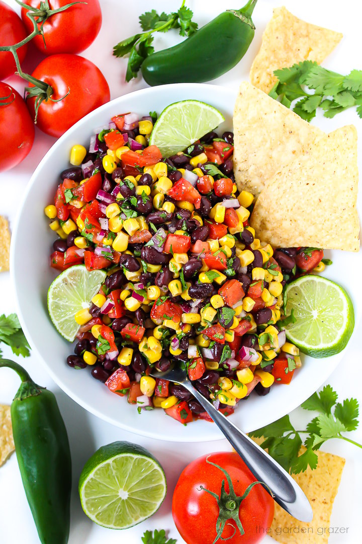 Black bean corn salsa in a white bowl with fresh lime slices and tortilla chips on the side