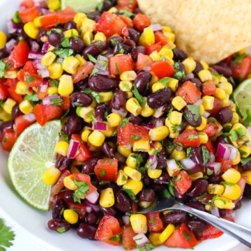 Close up view of black bean salsa in a white bowl with lime slice and serving spoon