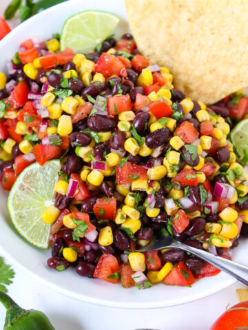 Close up view of black bean salsa in a white bowl with lime slice and serving spoon