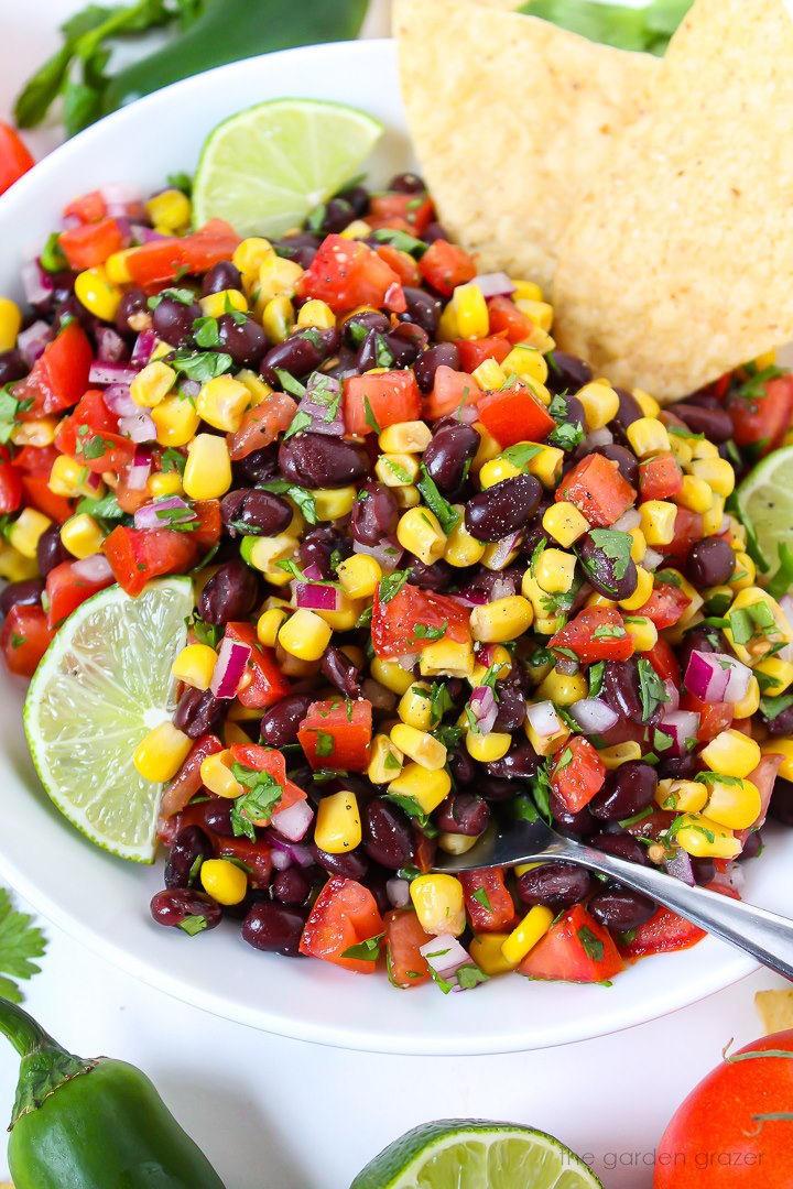 Close up view of black bean salsa in a white bowl with lime slice and serving spoon