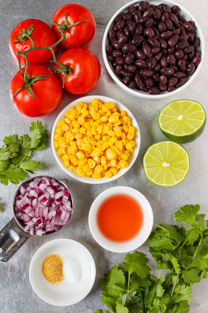Beans, sweet corn, tomatoes, lime, red onion, vinegar, and fresh herb ingredients laid out on a metal tray